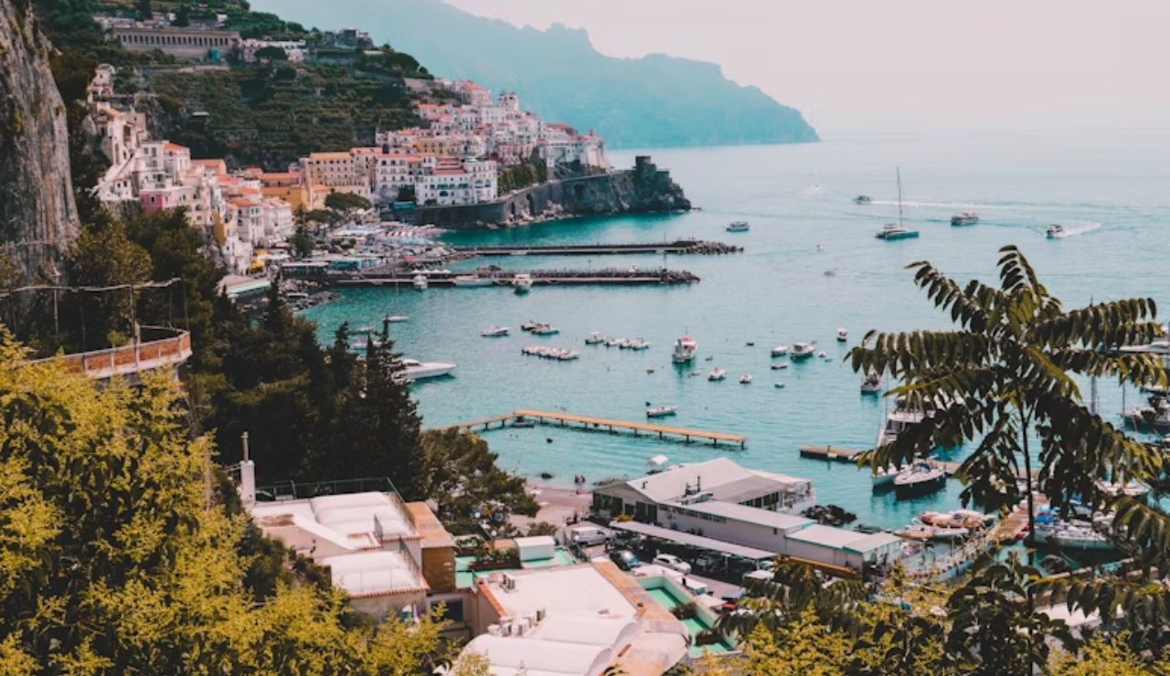 Colorful cliffside town of Amalfi, Italy, overlooking a marina filled with boats and the sparkling Tyrrhenian Sea.