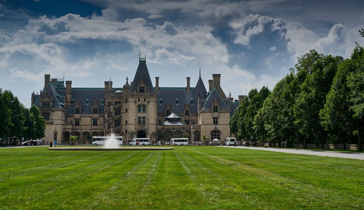 Front view of the historic Biltmore Estate in Asheville, North Carolina, with manicured lawns, a central fountain, and cloudy skies above.