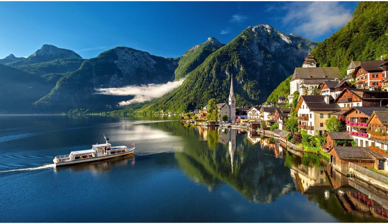 Scenic view of Hallstatt village with alpine mountains and a boat on the lake in Austria.