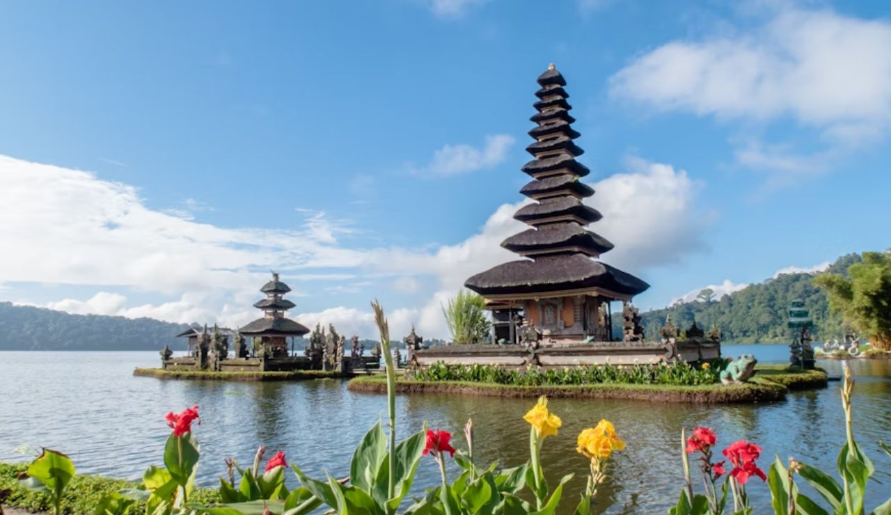 Ulun Danu Beratan Temple on Lake Beratan in Bali, Indonesia, with colorful flowers in the foreground and mountains in the background.