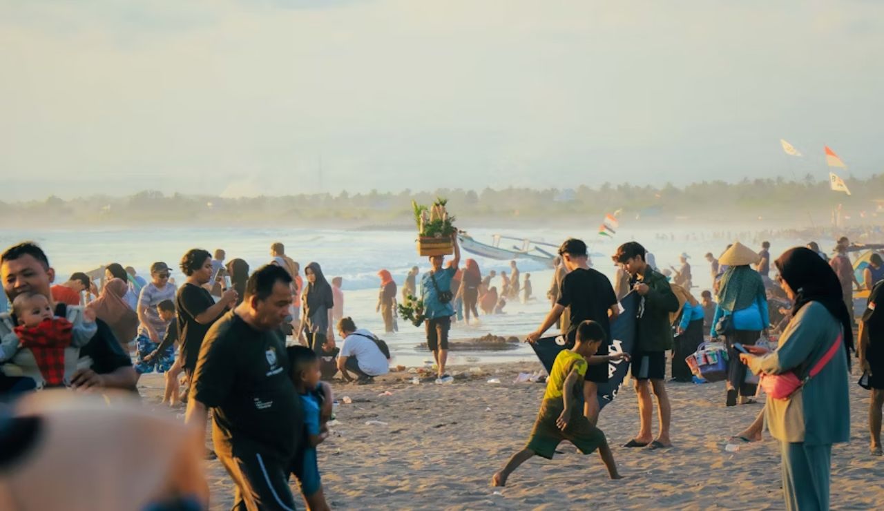 Crowds enjoy a lively day at the beach with families, vendors, and children playing by the shore.