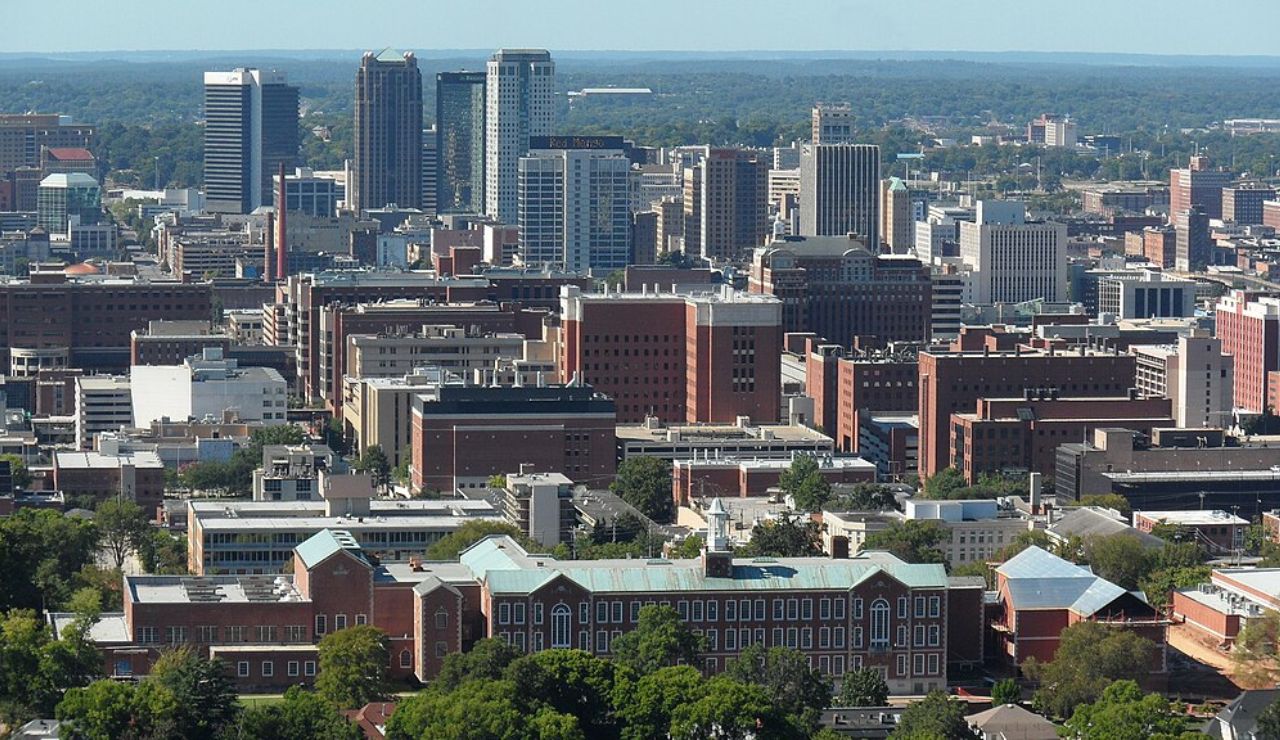 Aerial view of downtown Birmingham, Alabama, showcasing a mix of historic red-brick buildings and modern skyscrapers under a clear blue sky.