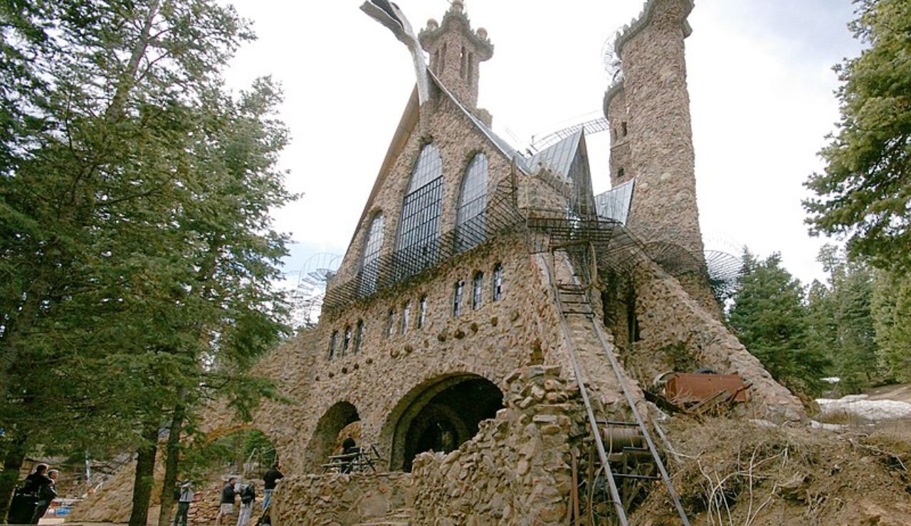 Bishop Castle in Colorado, a hand-built stone fortress with towering spires, iron bridges, and intricate metalwork, surrounded by pine trees and mountain terrain.
