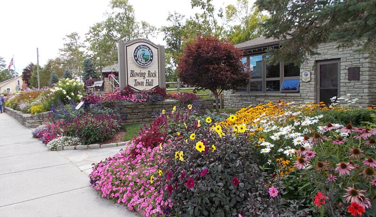 Colorful flower garden in front of Blowing Rock Town Hall in North Carolina with a stone building and town sign