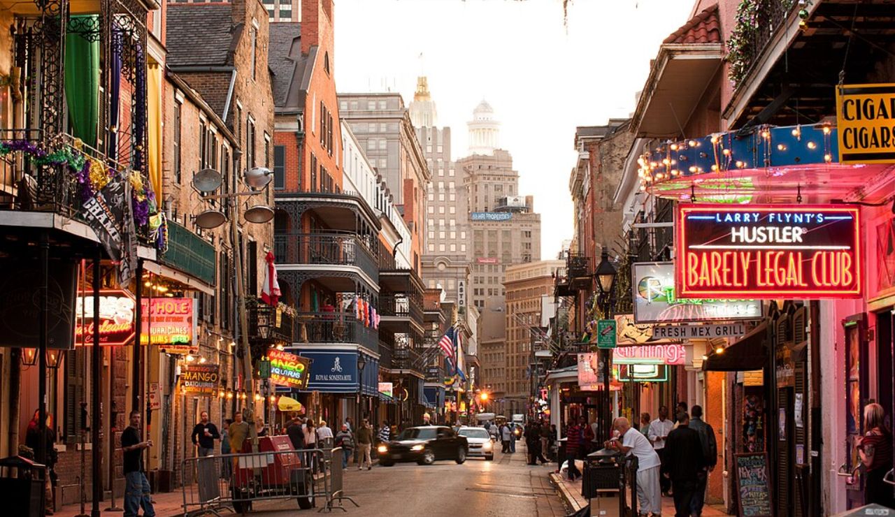 Evening view of Bourbon Street in New Orleans with neon signs, bars, historic buildings, and people walking along the vibrant street