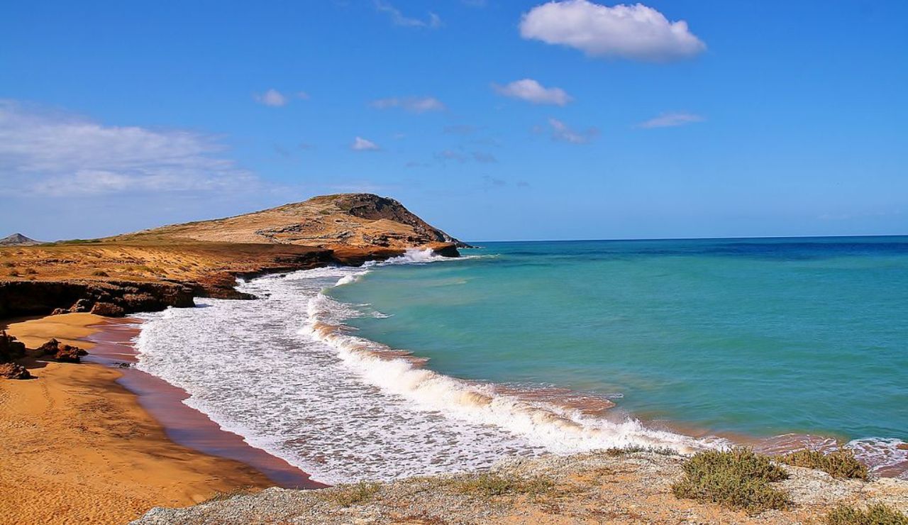 Golden sands and turquoise waters at Cabo de la Vela, Colombia, with rugged coastal cliffs and a clear blue sky in the background.
