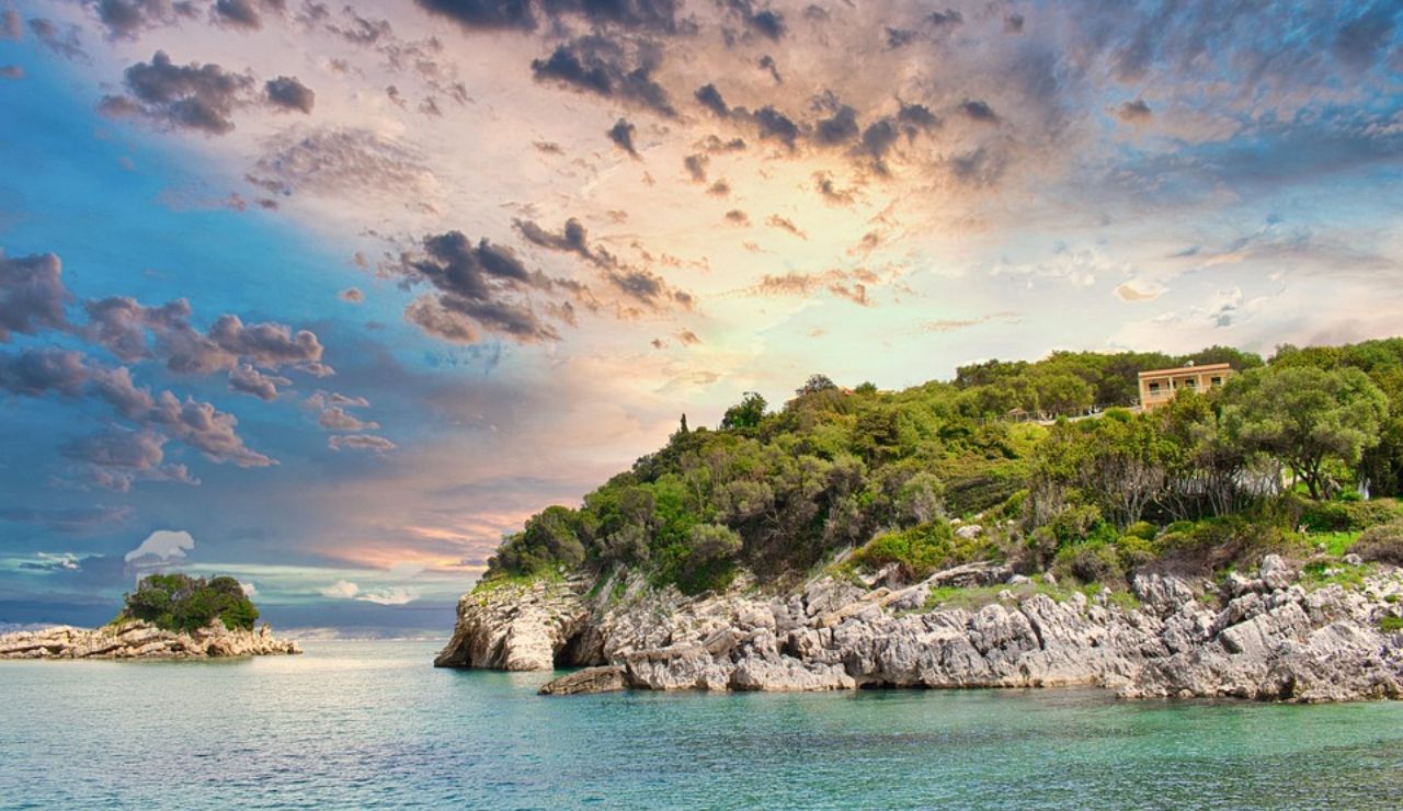 Rocky coastline with lush greenery and a colorful sunset over calm turquoise waters.