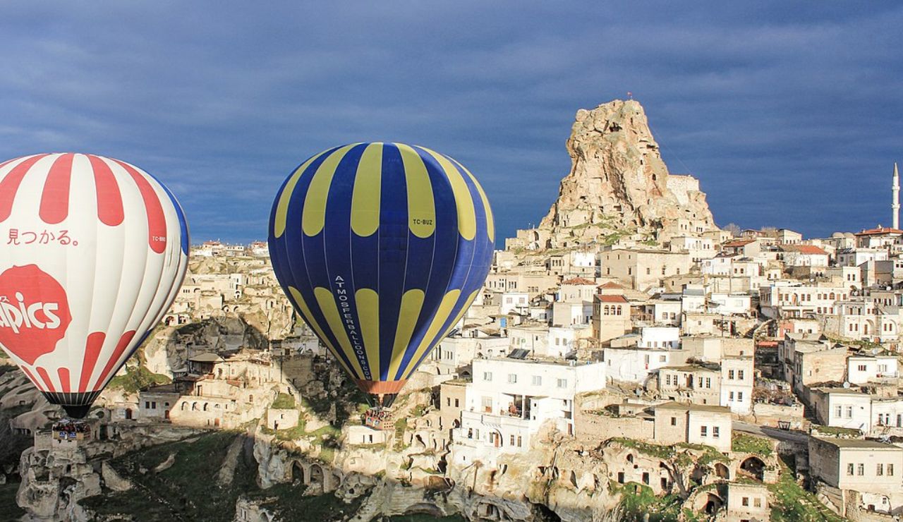 Colorful hot air balloons floating over the ancient cave dwellings and rock formations of Uçhisar, Cappadocia, Turkey, with Uçhisar Castle in the background.