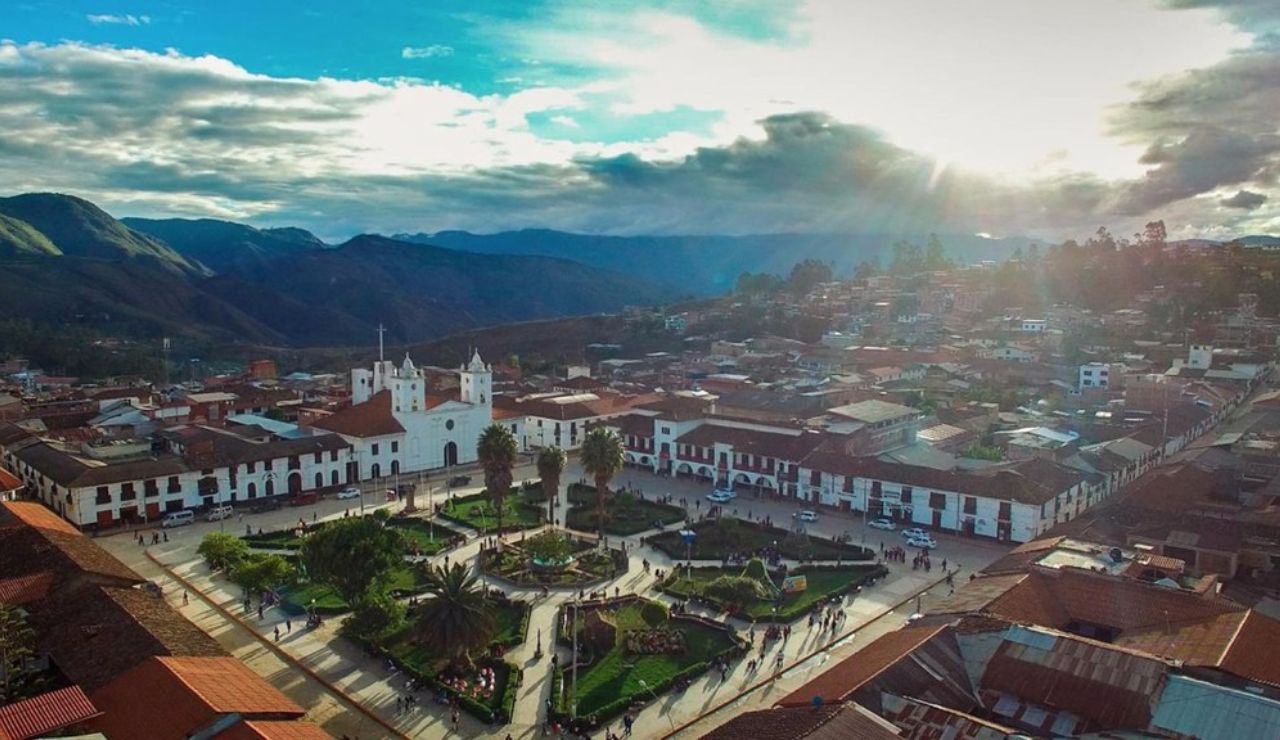 Aerial view of Chachapoyas, Peru, featuring the central Plaza de Armas with its colonial architecture, white church, and surrounding mountains under a dramatic sunset sky.