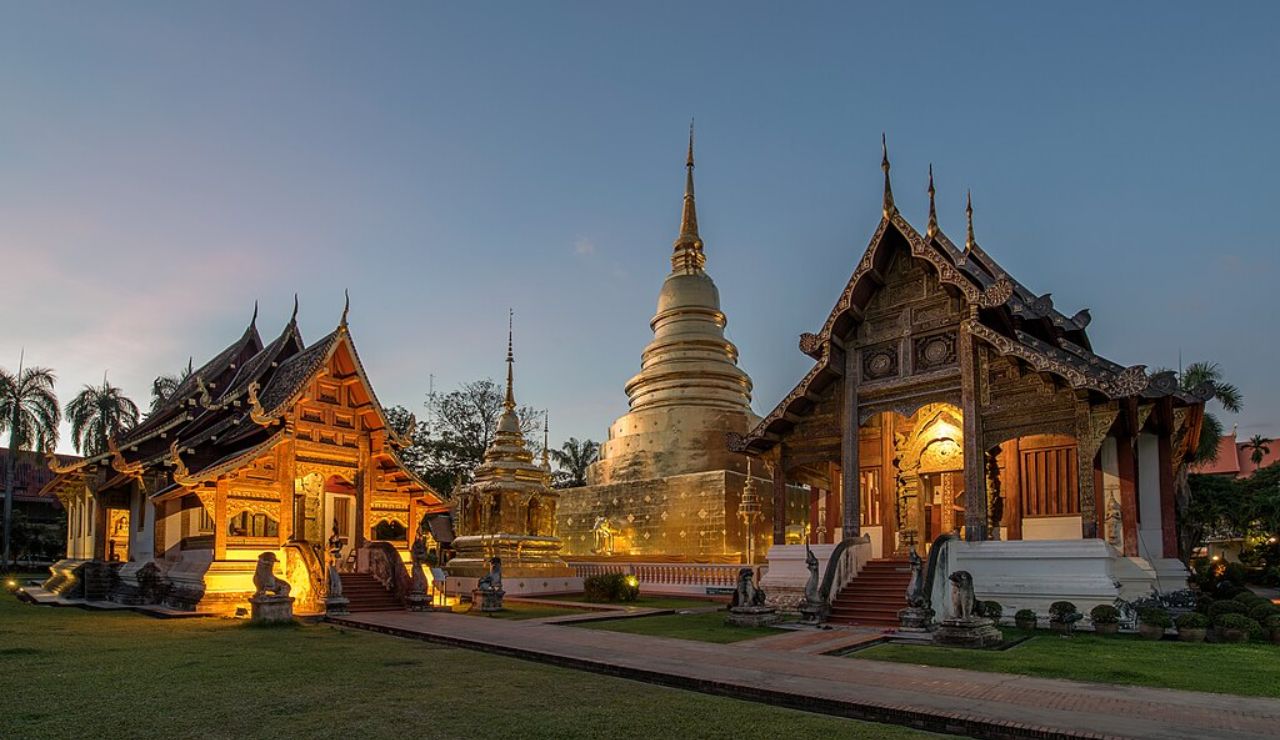 Wat Phra Singh temple complex in Chiang Mai, Thailand, illuminated at dusk with its ornate wooden structures and golden stupa.