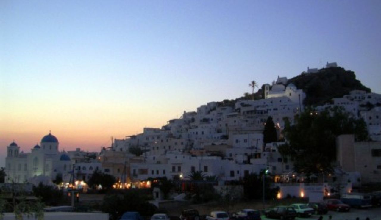 Whitewashed hillside houses and blue-domed church at dusk in Chora, Ios Island.