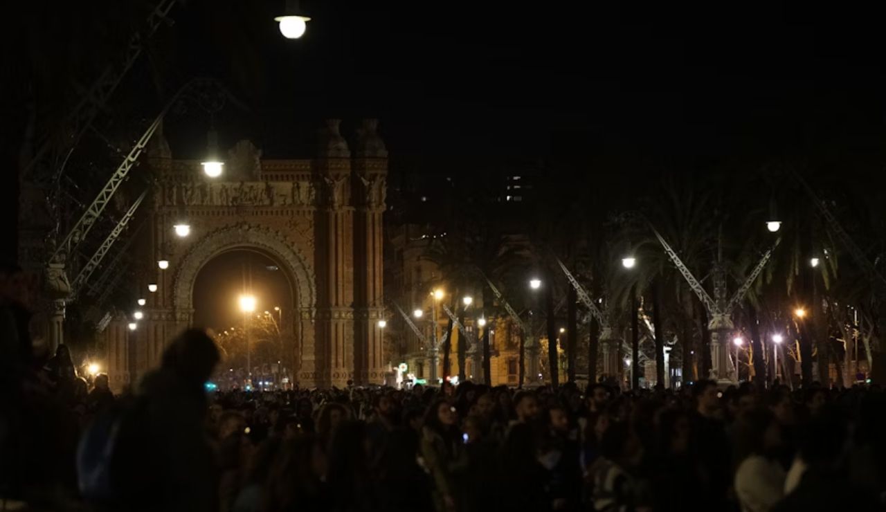 Crowd gathered at night near Arc de Triomf in Barcelona during anti-tourism protest.