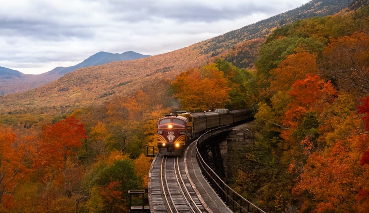 Fall foliage surrounds a scenic train crossing a bridge in the White Mountains, New Hampshire.