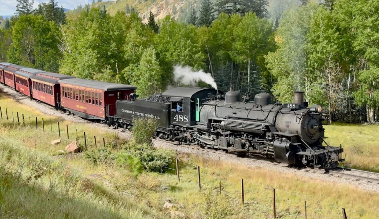 Historic steam locomotive of the Cumbres & Toltec Scenic Railroad traveling through forested hills in Colorado and New Mexico.