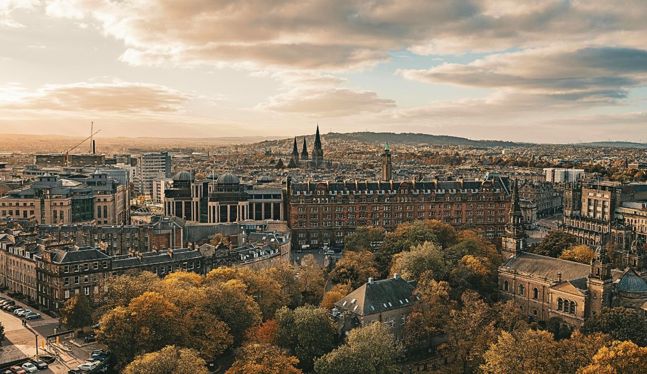 Edinburgh Castle viewed from a hilltop with surrounding stone buildings and Arthur’s Seat in the background under a cloudy sky.