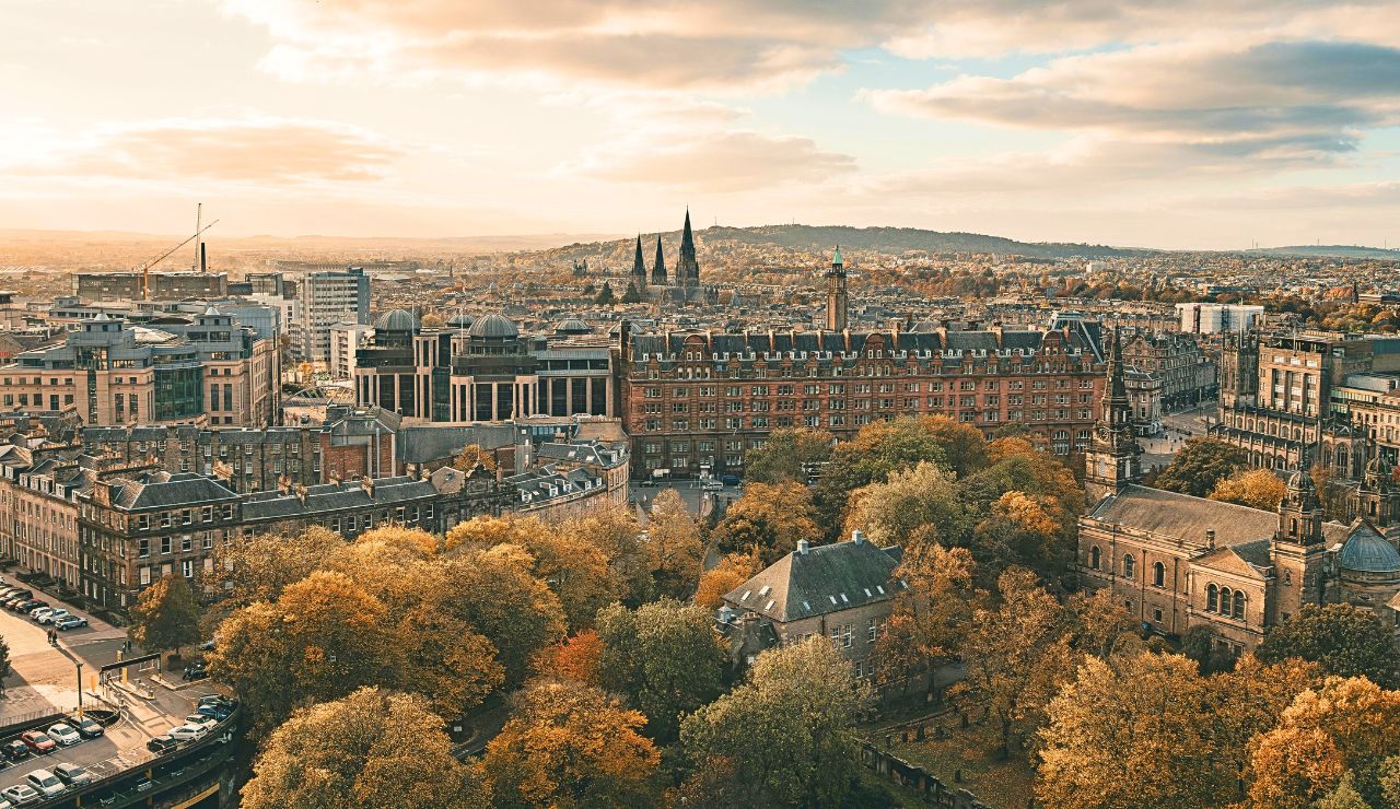Aerial view of a historic city with tree-lined streets and hills under a partly cloudy sky.