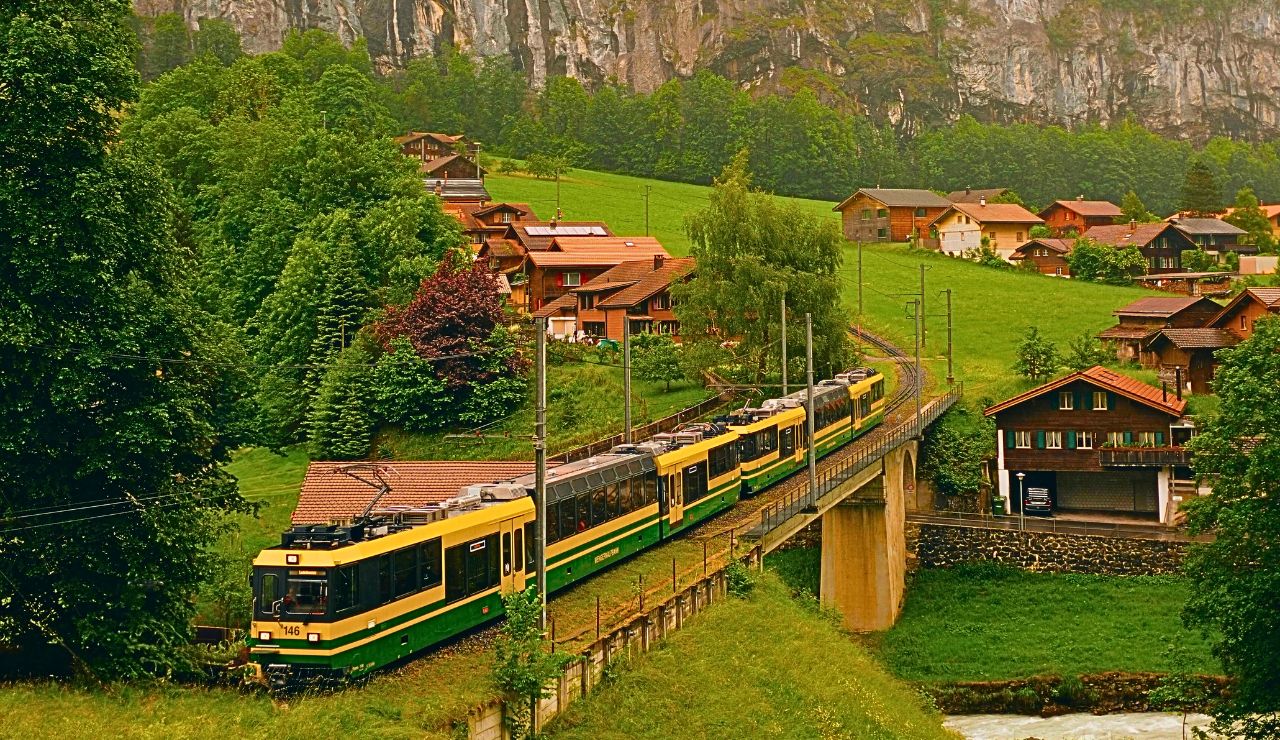 A small Feve train traveling through a lush green valley with mountains in the background.