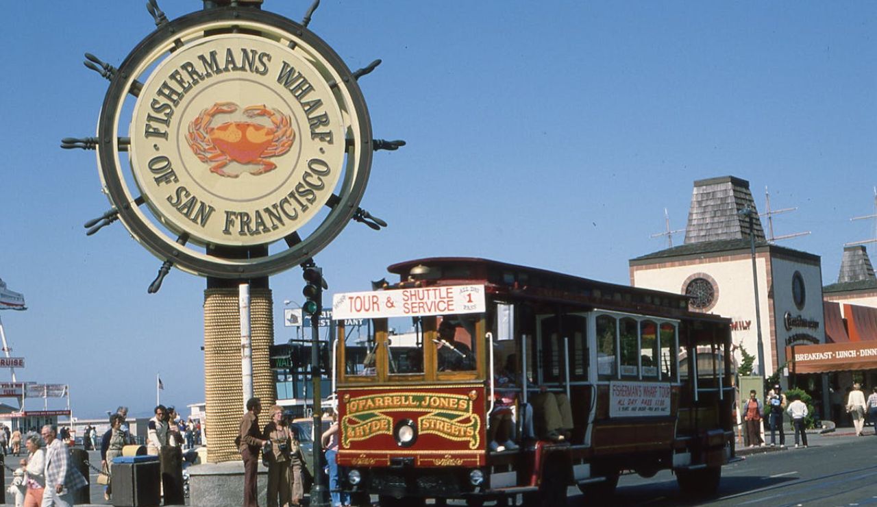 Fisherman’s Wharf sign in San Francisco with a historic cable car and tourists exploring the waterfront area on a sunny day