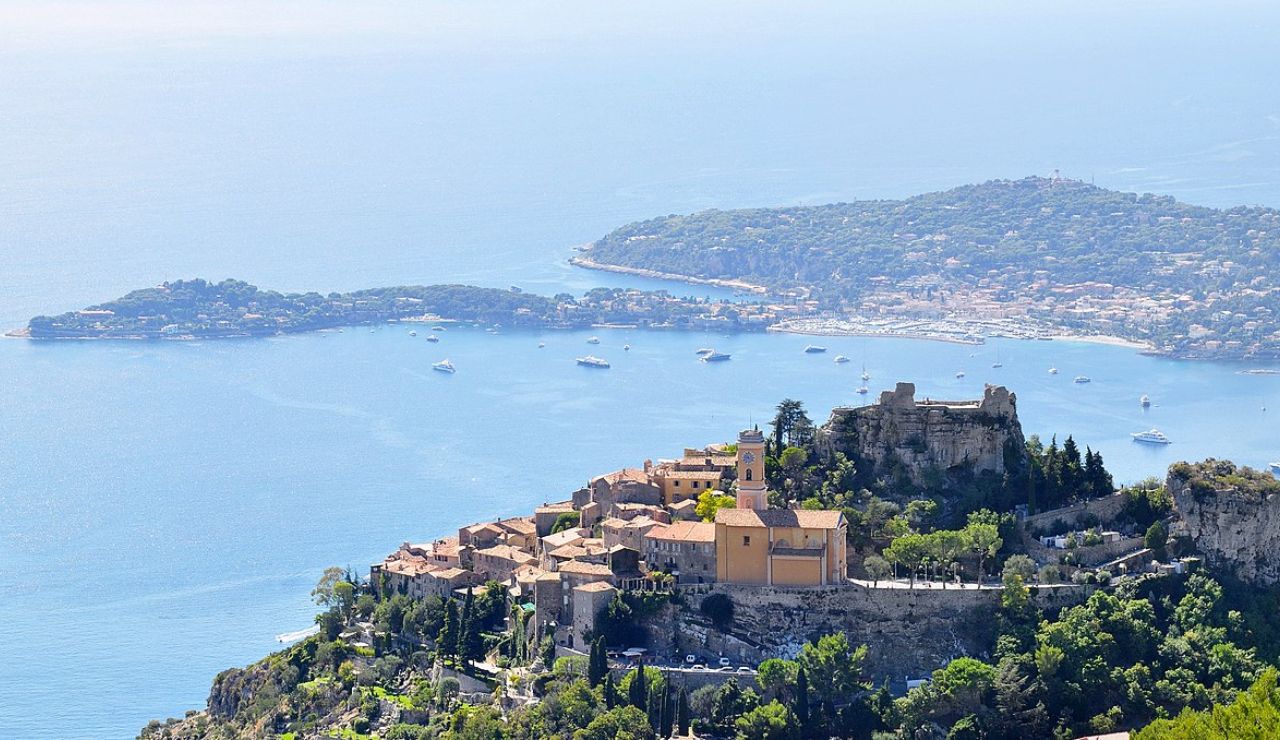Aerial view of the hilltop village of Èze in the French Riviera, with terracotta rooftops, a historic church, and the Mediterranean Sea in the background dotted with yachts.