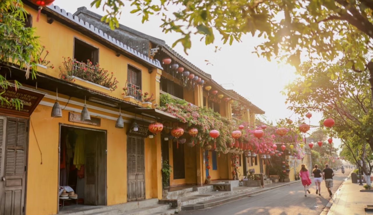 Charming street in Hoi An Ancient Town, Vietnam, with yellow colonial buildings, hanging lanterns, and blooming flowers at sunset.