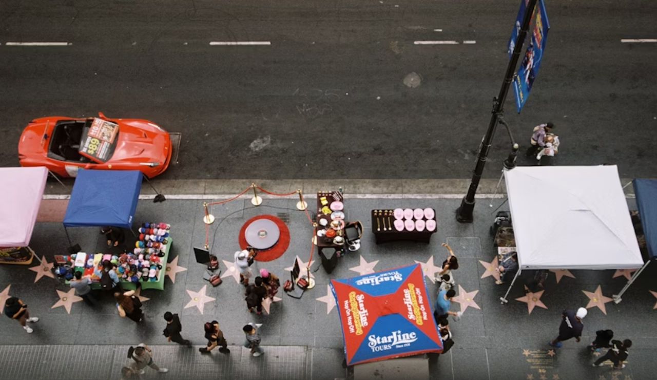 Overhead view of Hollywood Walk of Fame with street vendors, tourists, and a red sports car parked nearby