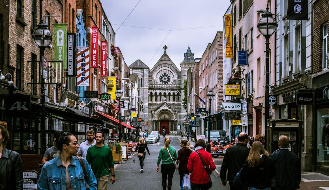 Pedestrians walking along a busy shopping street in Dublin, Ireland, with a historic church in the background.