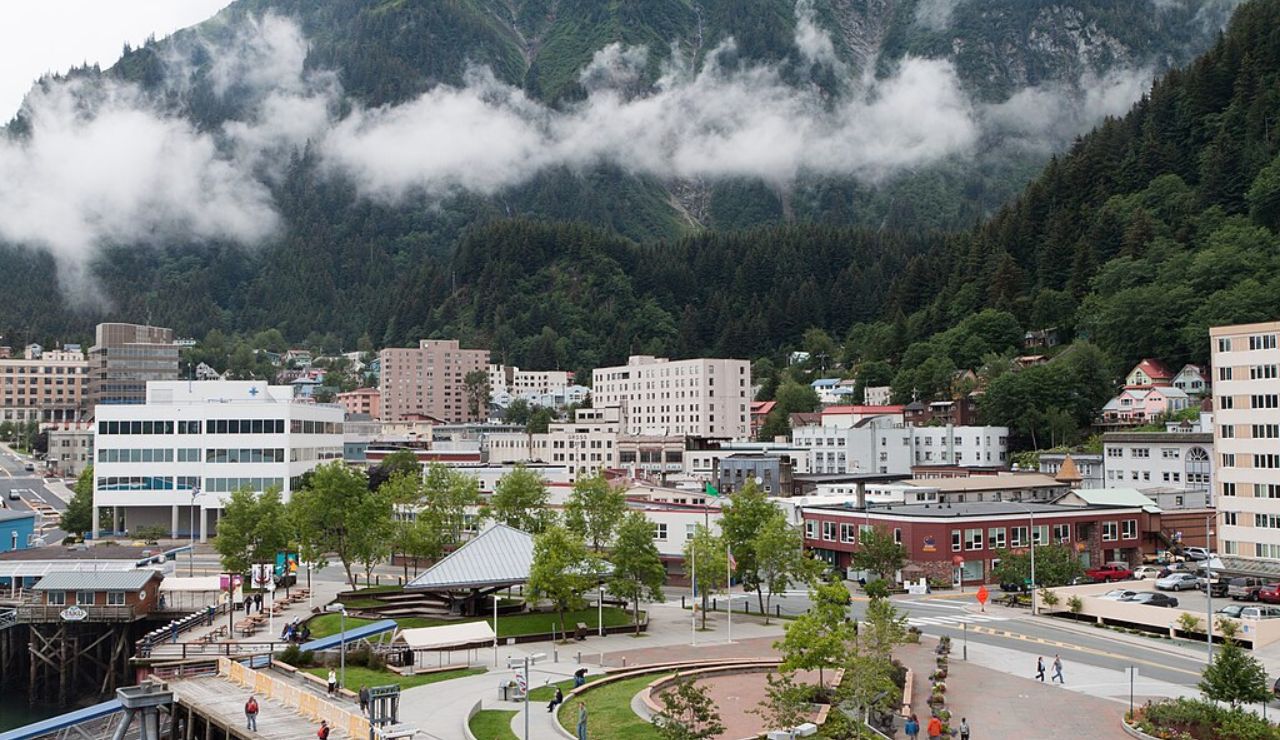Downtown Juneau, Alaska with modern buildings, lush green mountains, and low-hanging clouds on a misty day.