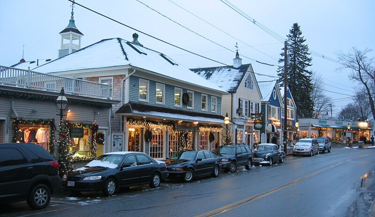 Charming small-town street with snow-covered rooftops, holiday lights, and parked cars on a winter evening