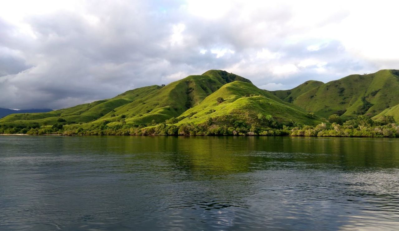 Green rolling hills reflecting on the calm waters of Komodo Island, Indonesia.