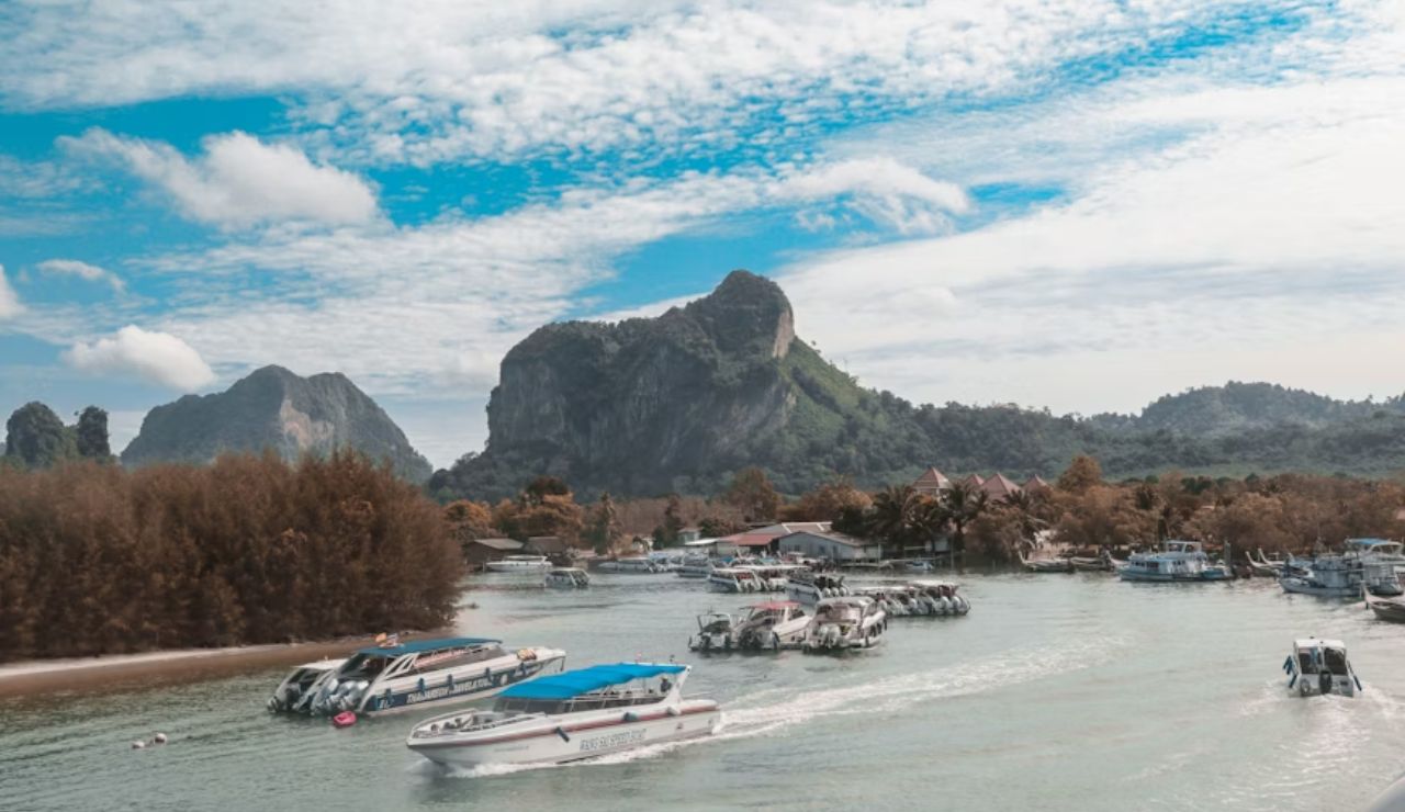 Speedboats docked along the coast with limestone cliffs in the background at Ao Nang, Krabi, Thailand, under a partly cloudy sky.