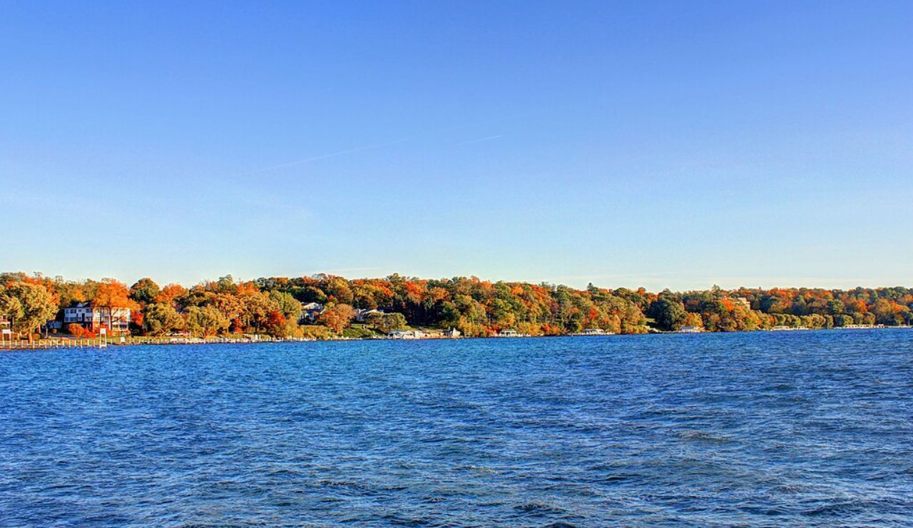 Scenic view of Lake Geneva in Wisconsin with vibrant autumn foliage, waterfront homes, and clear blue skies reflecting on the lake.