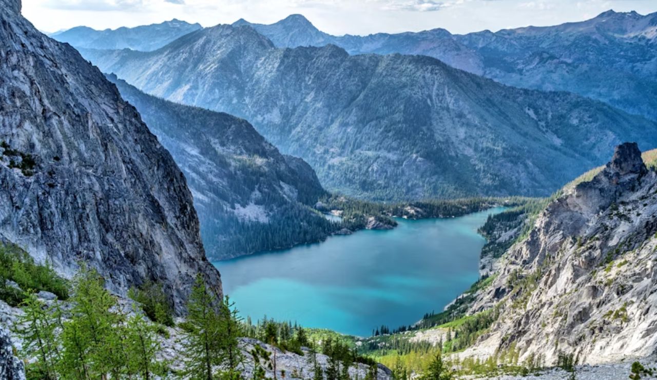 Scenic view of a turquoise alpine lake surrounded by rugged mountains and evergreen forests in the wilderness.