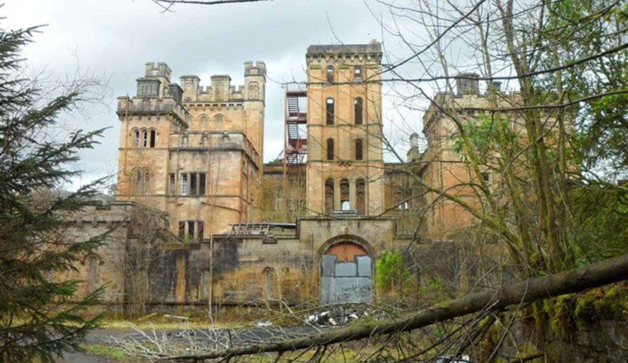Abandoned Lennox Castle in Scotland with overgrown trees and fallen branches.