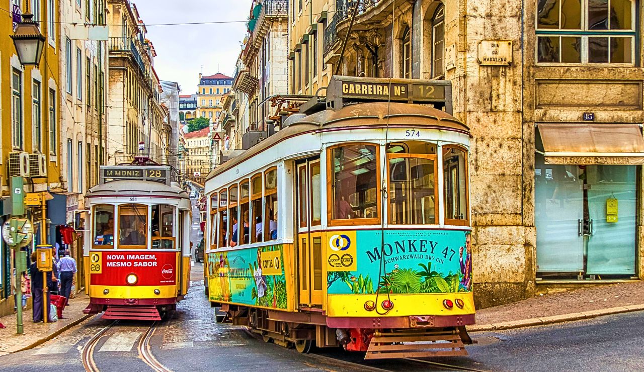 A yellow tram glides down a colorful Lisbon street lined with historic buildings and cobblestone paths.