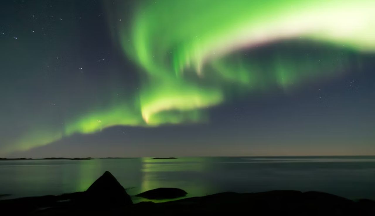 Vibrant northern lights dancing over calm coastal waters in the Lofoten Islands, Norway.