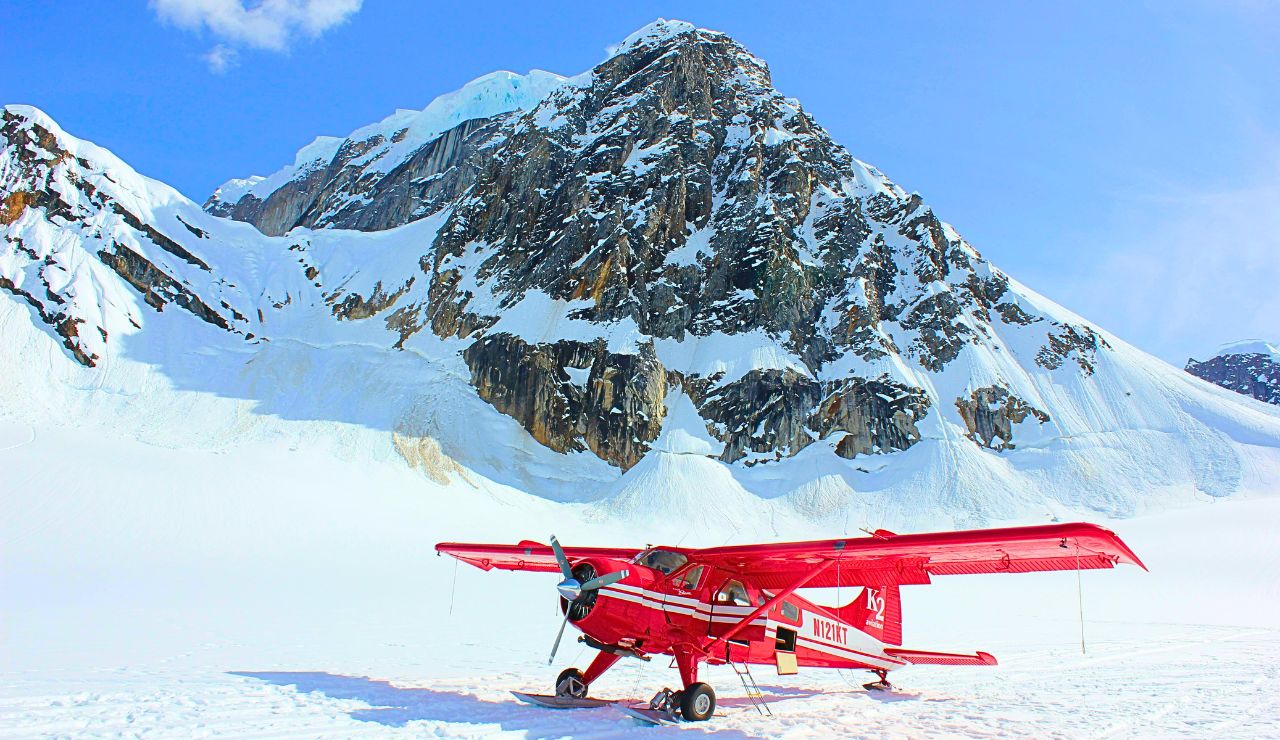 A floatplane flies over steep granite cliffs and blue lakes surrounded by evergreen forest in Misty Fjords National Monument.