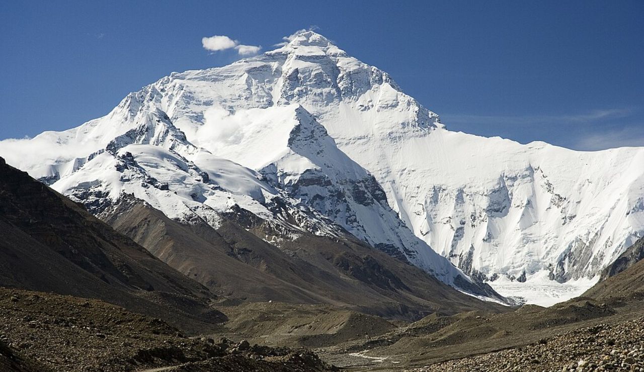 View of Mount Everest from Tibet's north base camp with snow-covered peaks and rocky foreground under a clear blue sky.
