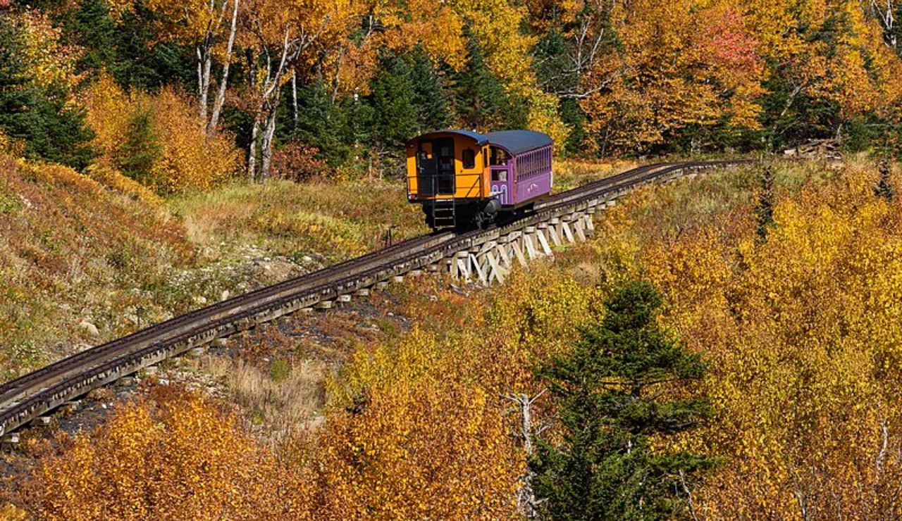 Colorful cog railway train ascending Mount Washington during fall foliage in New Hampshire.