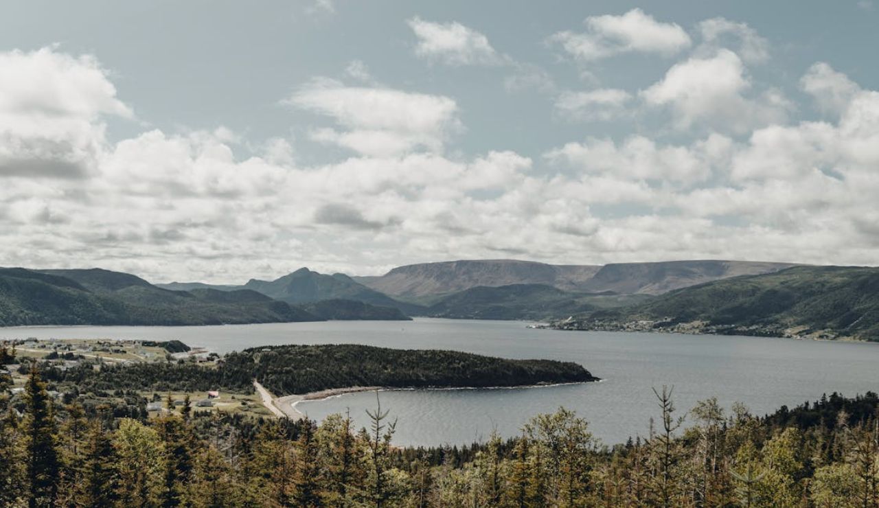 Scenic view of Gros Morne National Park in Newfoundland, Canada, with forested hills, a coastal bay, and cloudy skies.