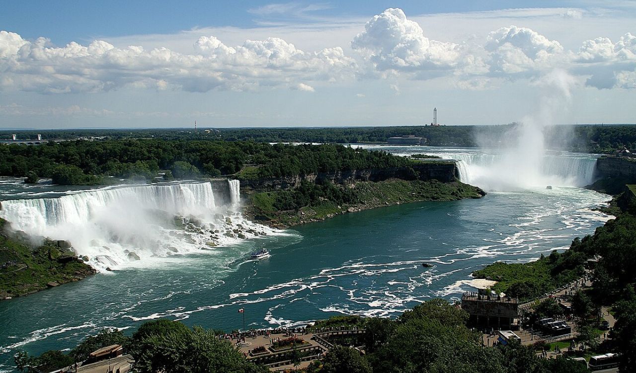 Powerful twin waterfalls cascade into a wide river below, surrounded by lush greenery and mist rising into the sky.