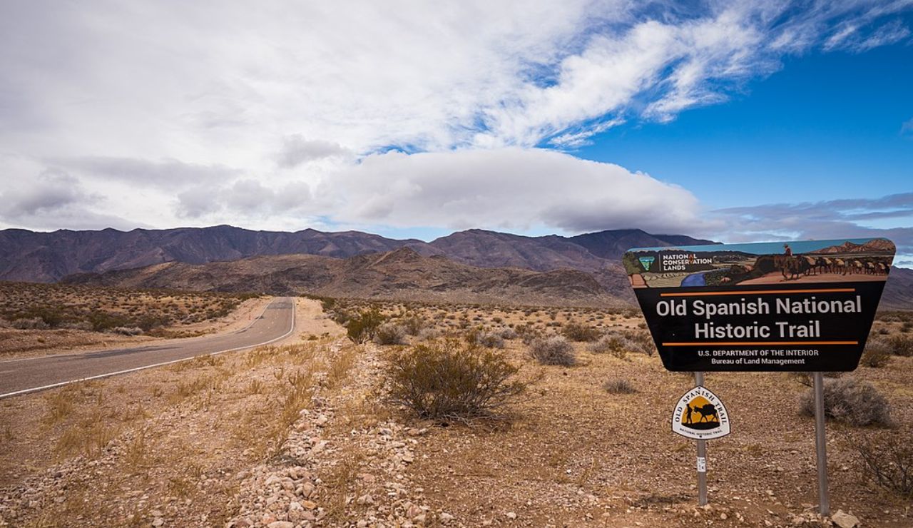 Sign for Old Spanish National Historic Trail with desert landscape and mountains in the background.