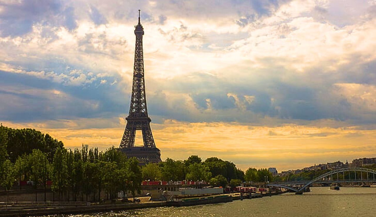 A couple walking hand in hand by the Seine River with the Eiffel Tower in the background.