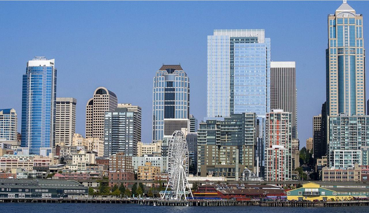 Seattle waterfront skyline featuring modern high-rise buildings and the Seattle Great Wheel on a clear sunny day.