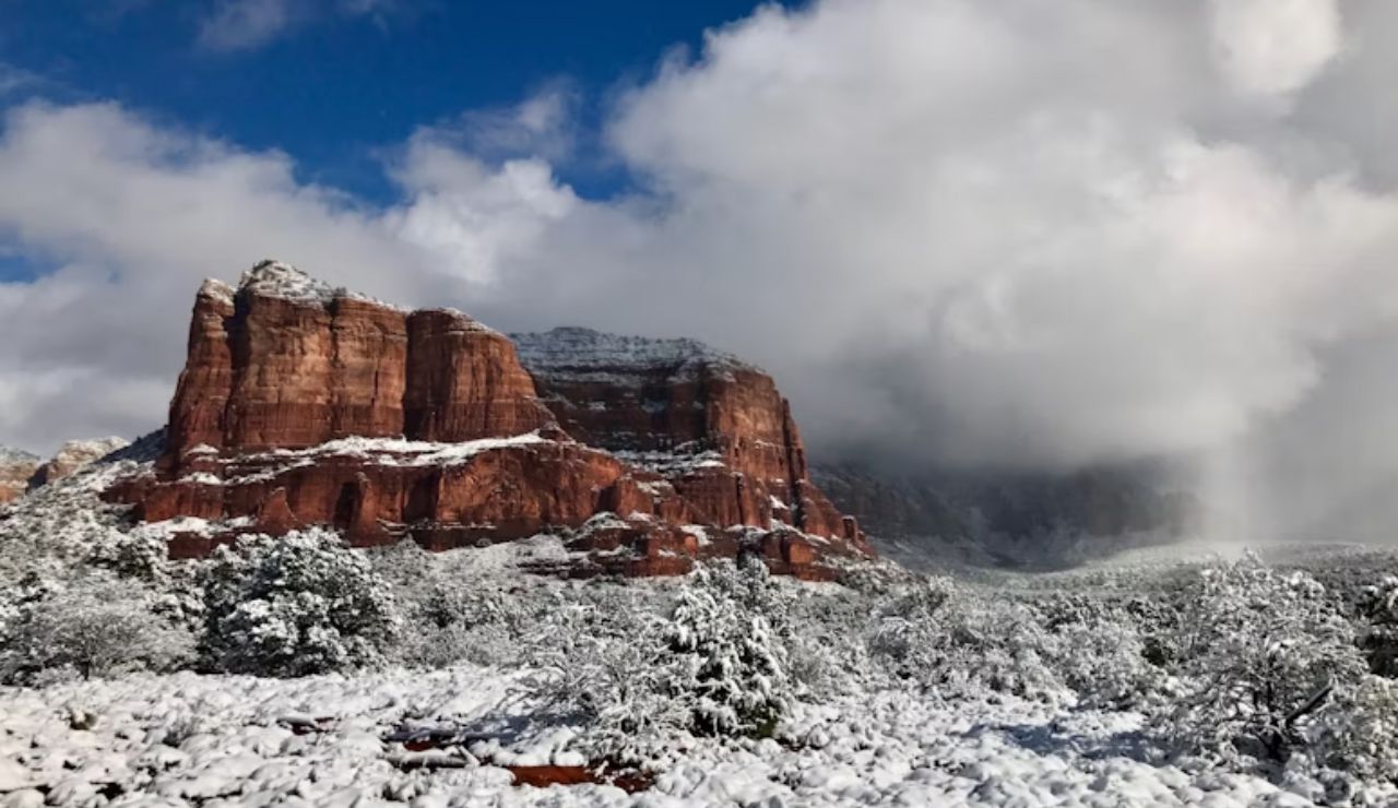 Snow-covered red rock formations and desert landscape in Sedona, Arizona under dramatic winter clouds and blue sky