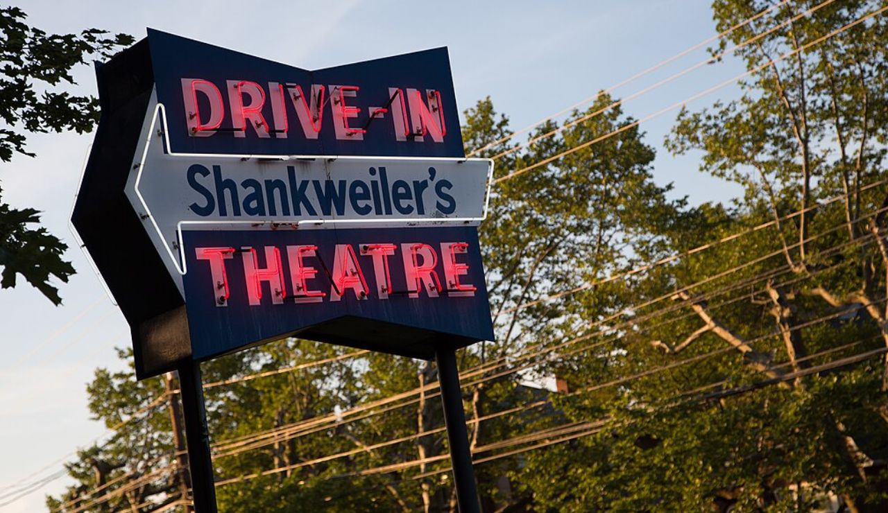 Vintage neon sign for Shankweiler's Drive-In Theatre, the oldest operating drive-in in the U.S., surrounded by trees and power lines at sunset.