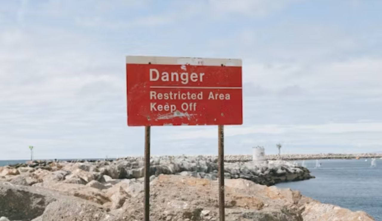 Red warning sign reading 'Danger Restricted Area Keep Off' near rocky shoreline
