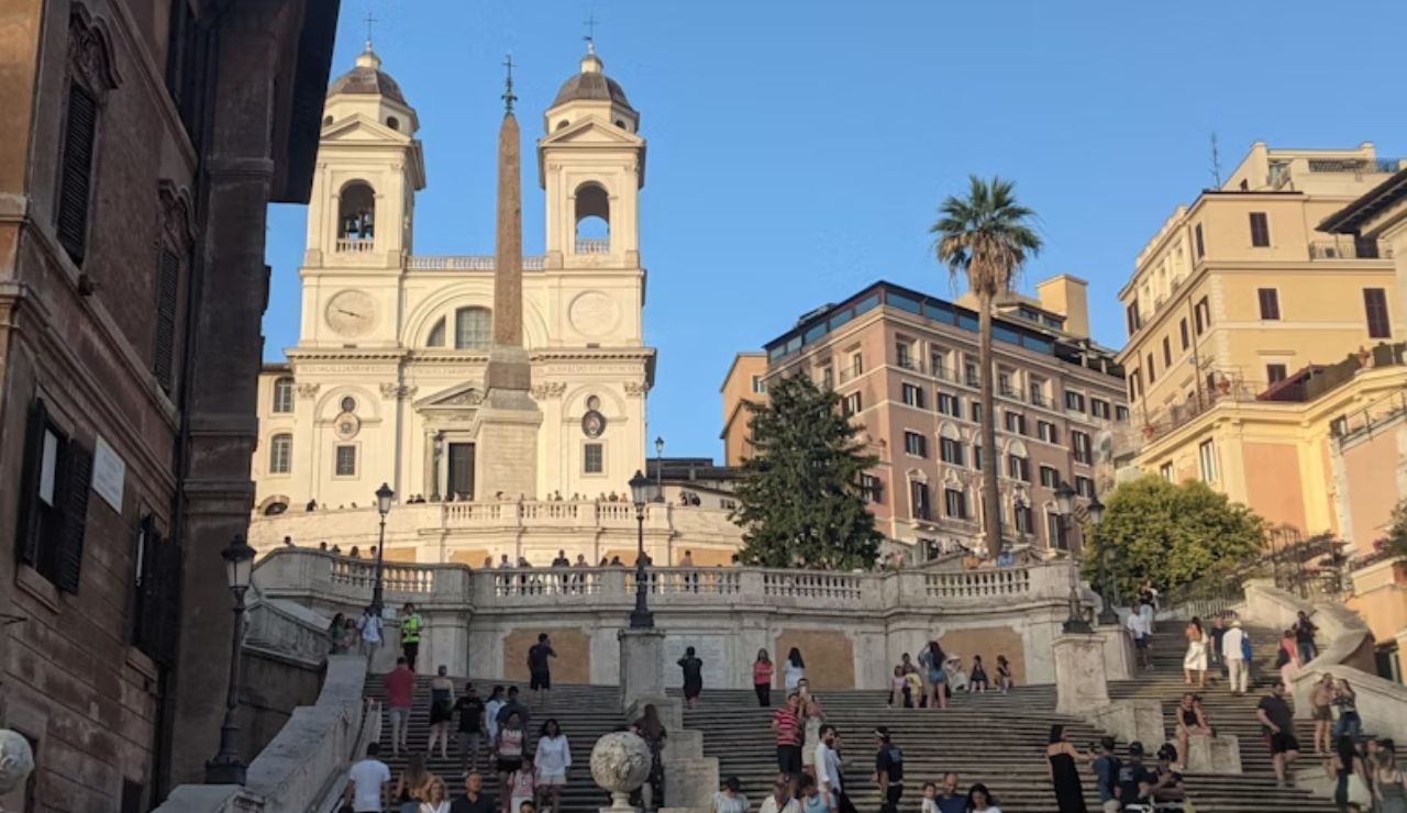 Tourists gather and relax on the iconic Spanish Steps in Rome under a clear blue sky.