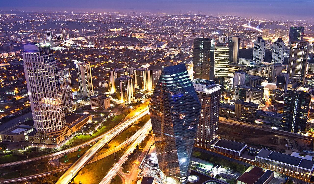 A vibrant cityscape at dusk, filled with glowing skyscrapers, busy roads, and lights stretching to the horizon.