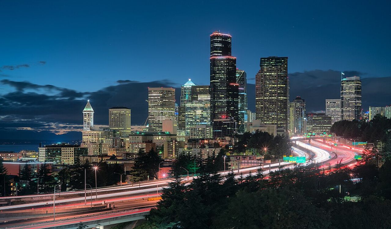 City lights glow as cars streak past on a lively highway at dusk.