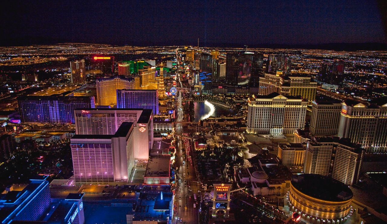 Aerial night view of the Las Vegas Strip with brightly lit casinos, hotels, and city lights stretching into the distance.